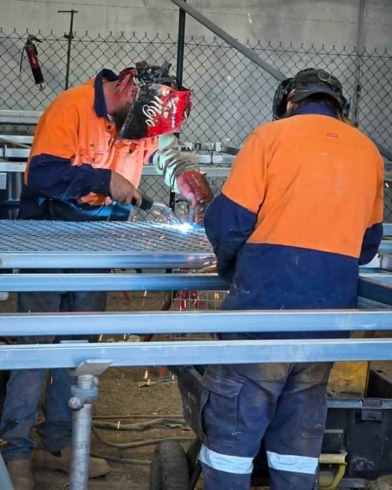 two fabricators in hi-vis welding galvanised steel mesh panels for a horse stable frame