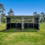 Outdoor steel animal shelter with two bays on grassy field