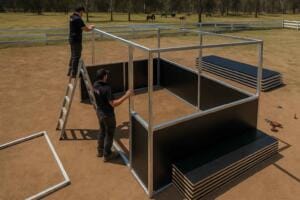 Two men assembling metal structure in open field.