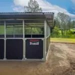 Steel horse stables beside lush green landscape.