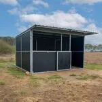 Metal shelter in open grassy field under blue sky.