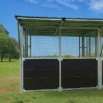 Outdoor kennel with mesh fencing in grassy field.