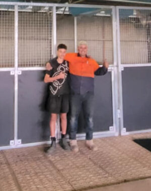 Two people smiling in front of metal enclosure.