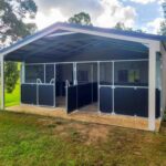 Modern outdoor horse stables in green landscape.