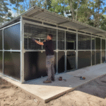 Man constructing outdoor animal shelter with black panels.