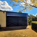 Compact steel stable shed with cross-braced barn doors on a rural property.