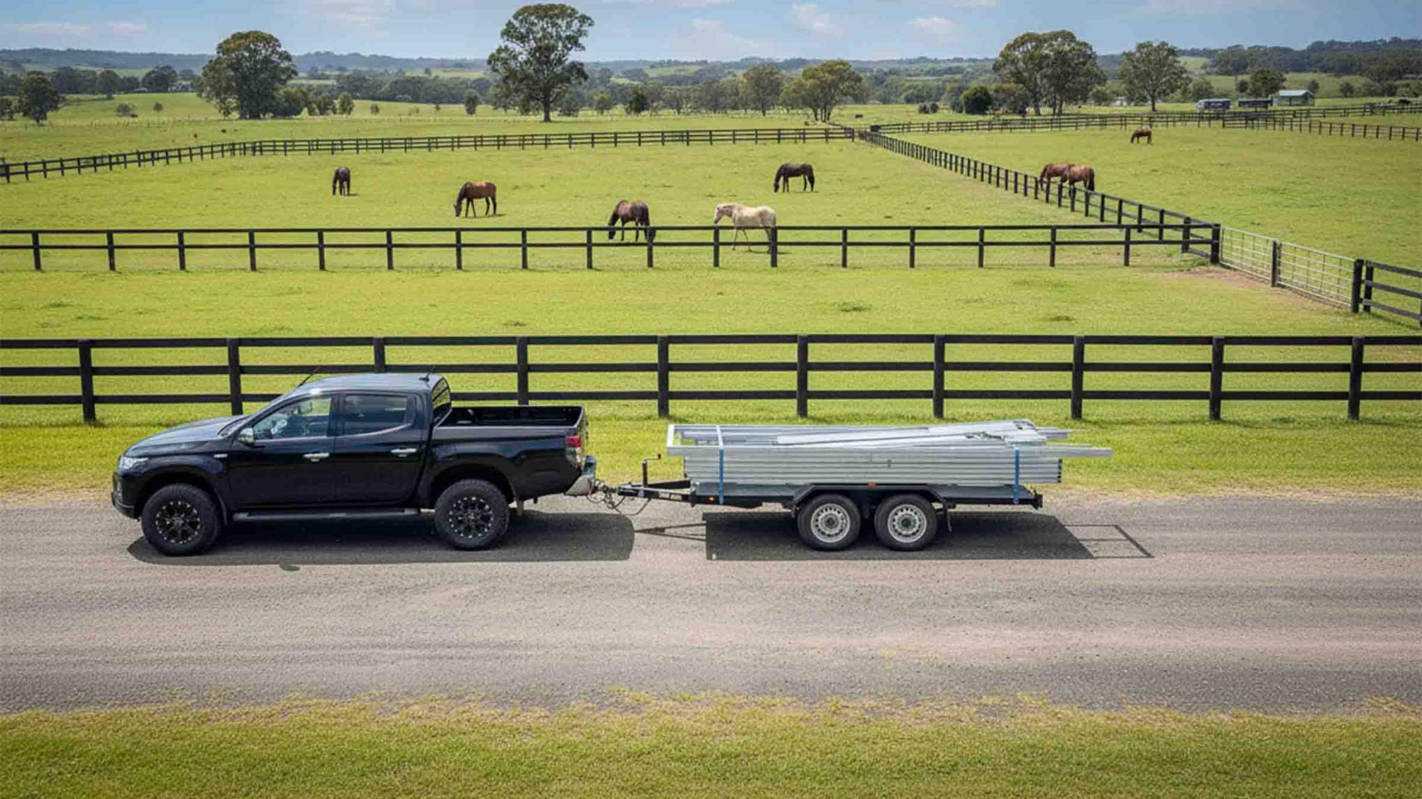 Ute towing trailer with flat pack stable on country road, horses in paddock.