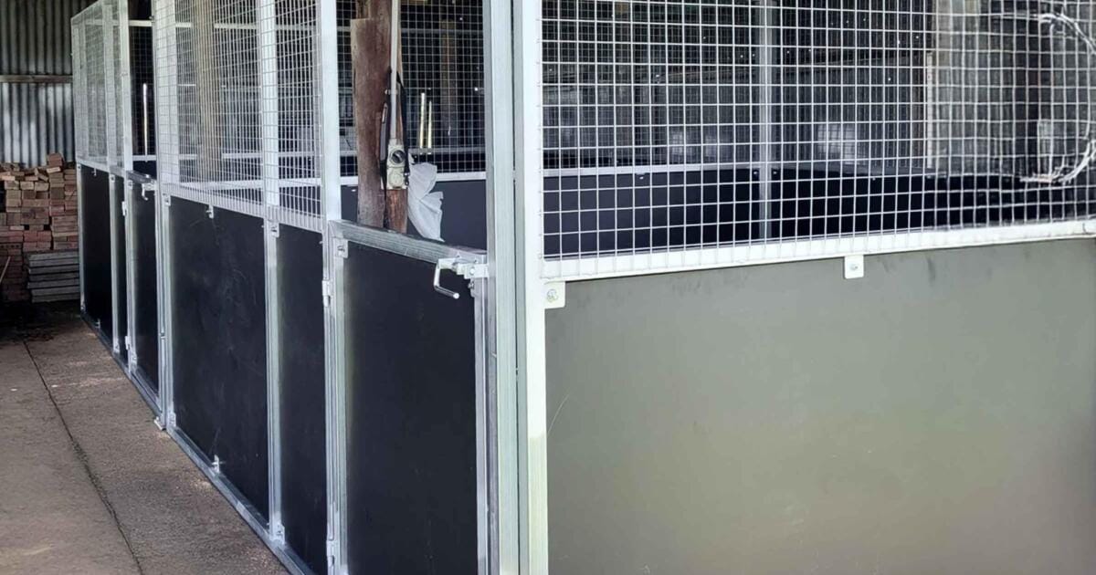 Empty horse stables with metal fencing indoors.