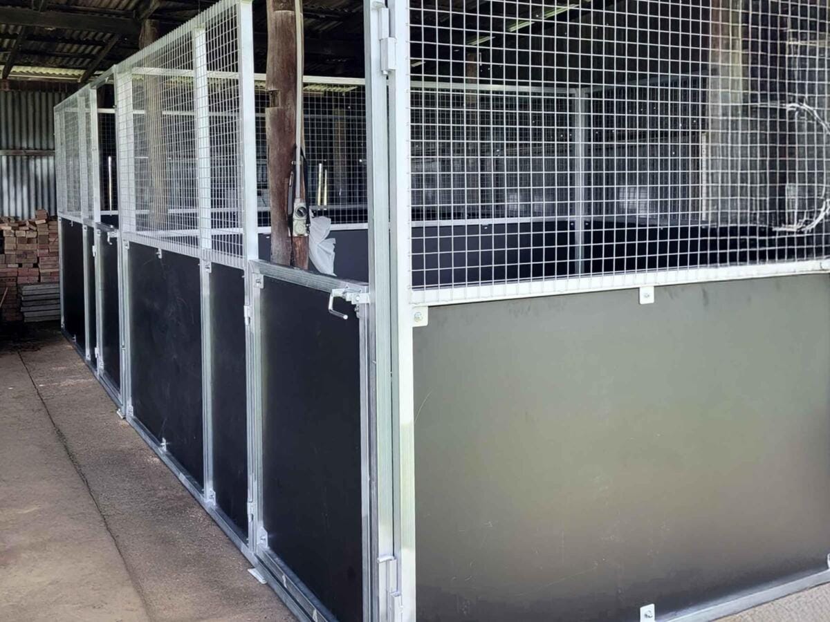 Empty horse stables with metal fencing indoors.