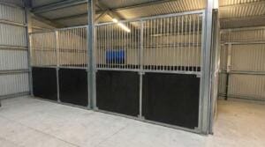 Rear interior view of modular stable system inside metal shed, showing vertical bar upper panels and form ply lower sections.
