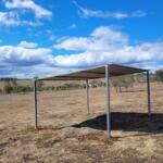 Metal shed on dry rural landscape under blue sky.