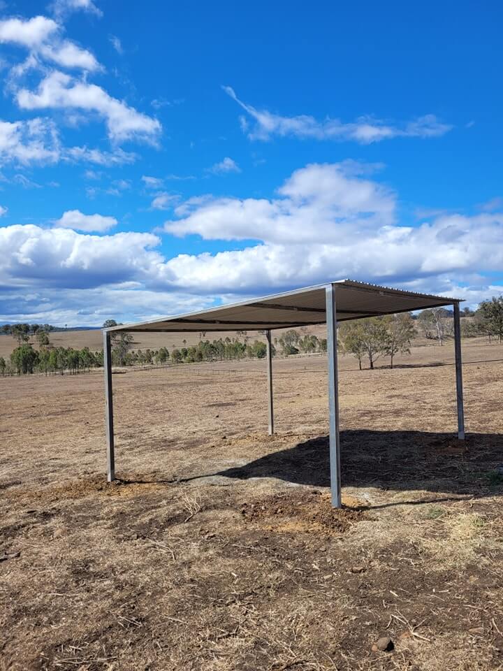 Metal shed on dry rural landscape under blue sky.