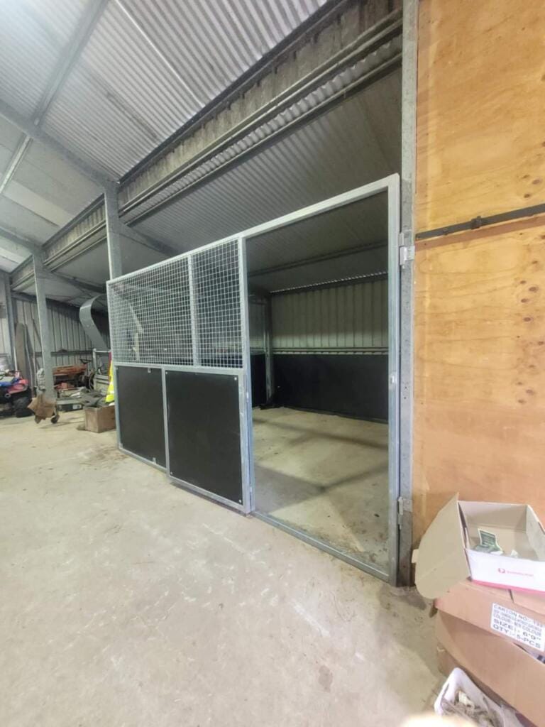 Empty metal animal pen inside a large shed