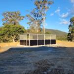Twin adjoining horse stables with pitched roof and mesh-top airflow panels on concretedbase.