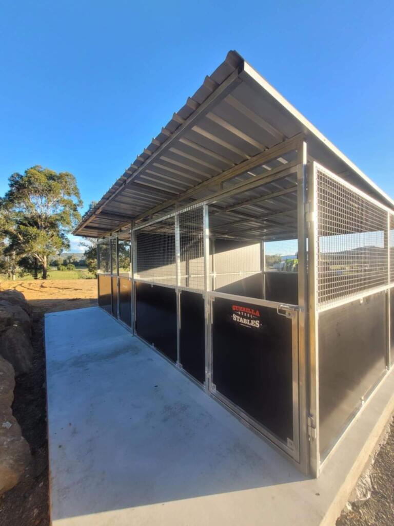 Outdoor horse stable with metal roof and fencing.