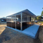 Twin welded horse stables on concrete-ready base with extended roof coverage.