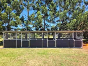 three  bay steel horse stable structure with mesh panels and galvanised frame under rural trees