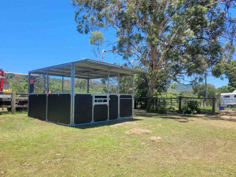 Outdoor steel horse stable bay featuring custom tie-up rail and feeding hatch on gate