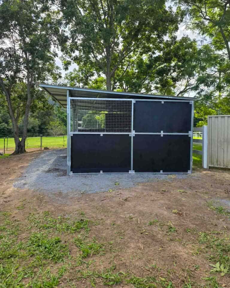Two-bay shelter with split mesh and ply walls beside a gravel yard